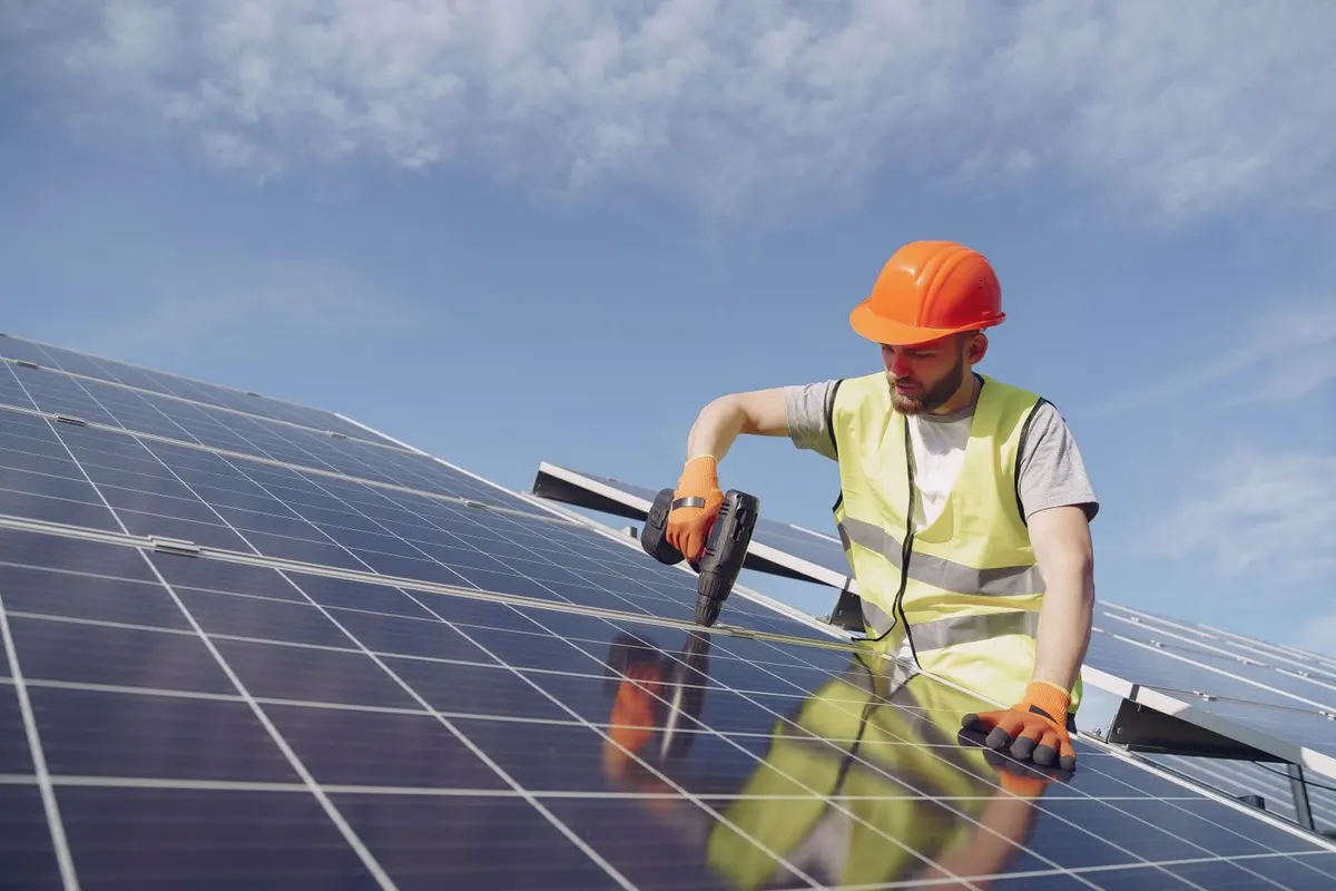 Tehnician montând un panou fotovoltaic pe acoperiș, sub cer senin